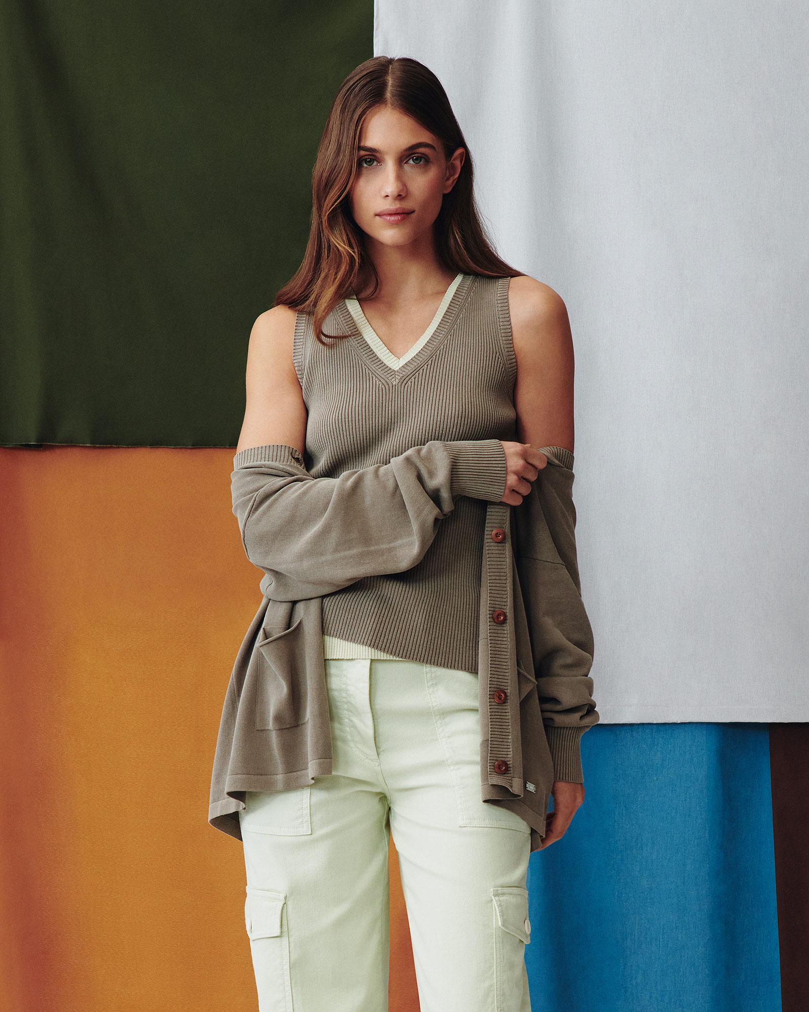 Mujer con top beige y cárdigan a juego frente a un fondo colorido.