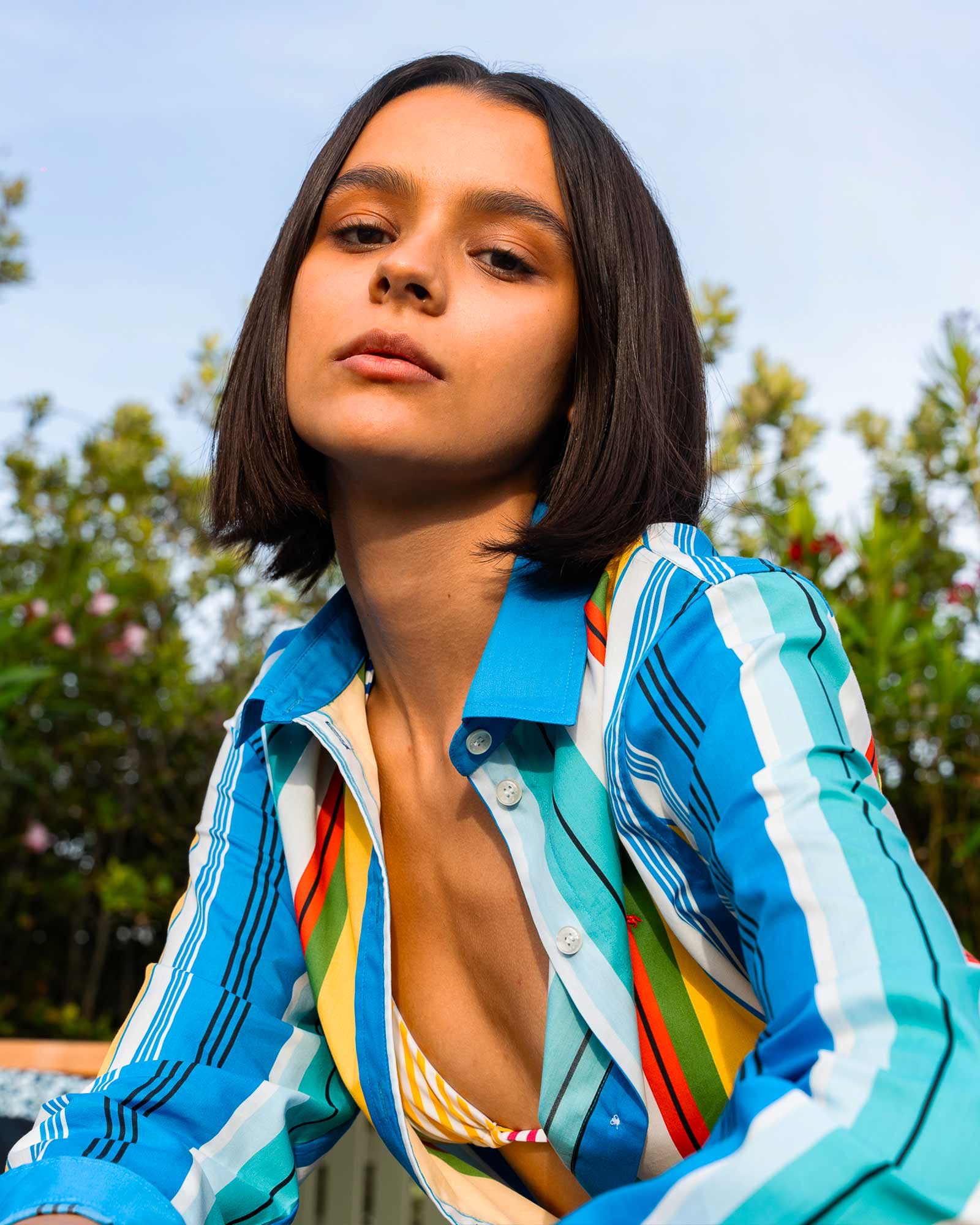 Mujer con camisa de rayas multicolor y bikini amarillo, entre plantas.