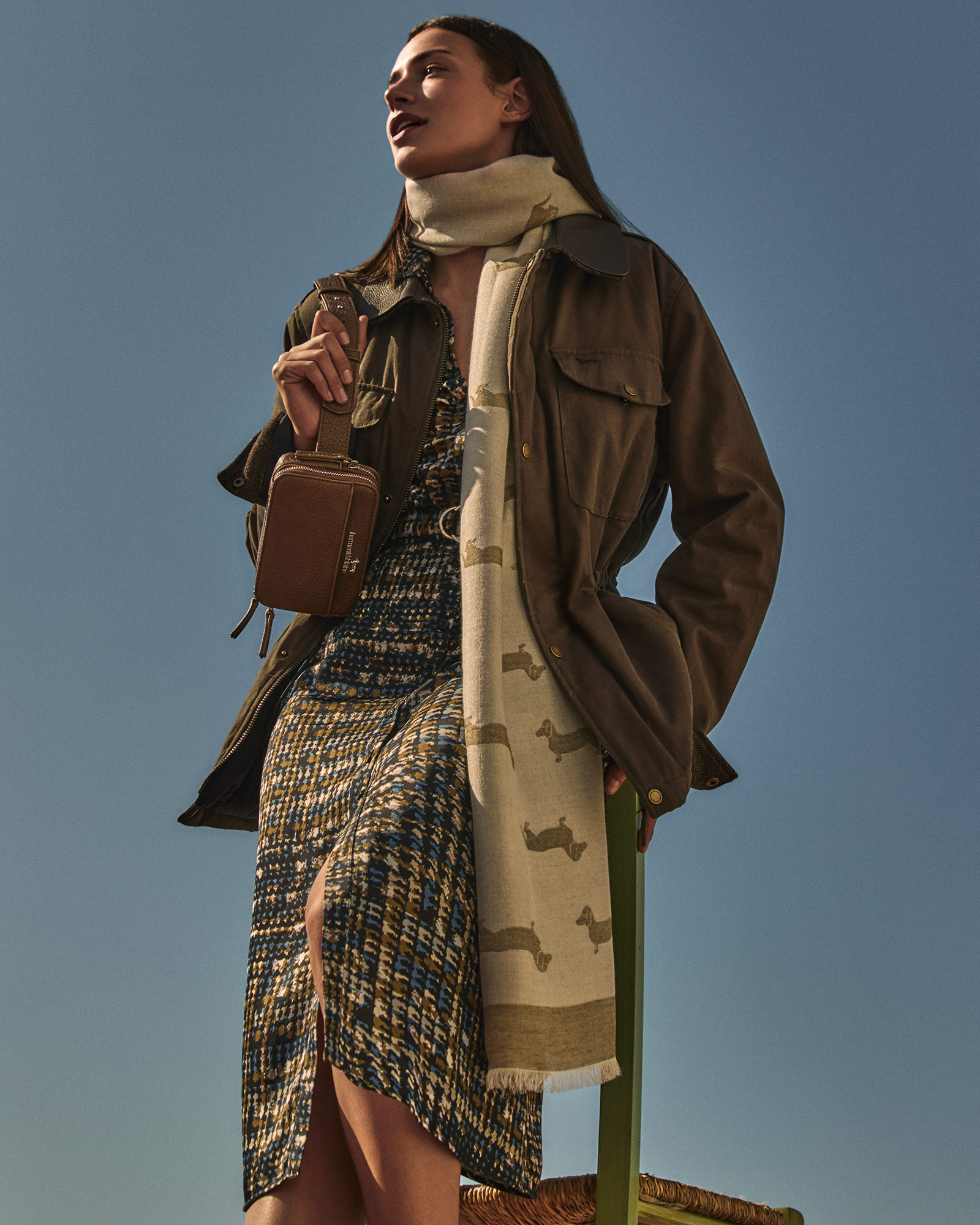 Woman wearing olive military jacket, tweed dress and brown bag