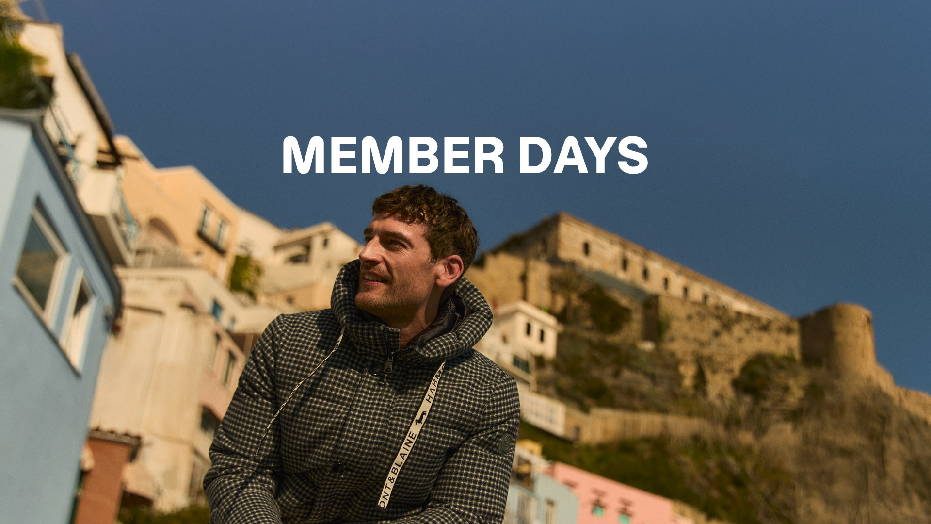 Coppia che iDue persone in posa all&rsquo;aperto davanti a un edificio con archi, indossano capi invernali Harmont & Blaine. Testo &lsquo;MEMBER DAYS&rsquo; in alto, immagine che promuove l&rsquo;anticipo dei saldi riservato ai clienti registrati.ndossa cappotti invernali davanti a un grande fiore blu.