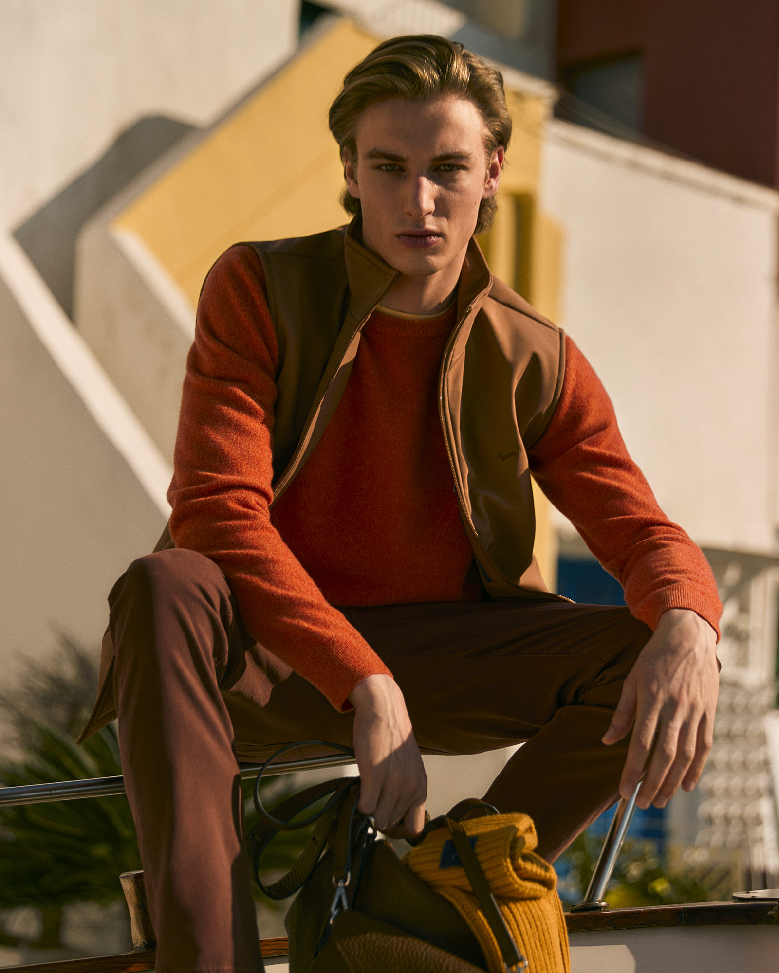 Hombre con suéter naranja y chaleco marrón, sentado en un barco.