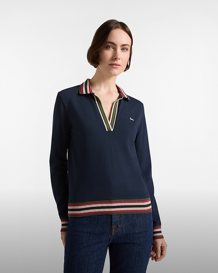 A woman with short brown hair wearing a women's dark blue long-sleeved polo shirt with a deep V-neck, multicoloured striped details on the collar, cuffs, and hem, paired with dark jeans.