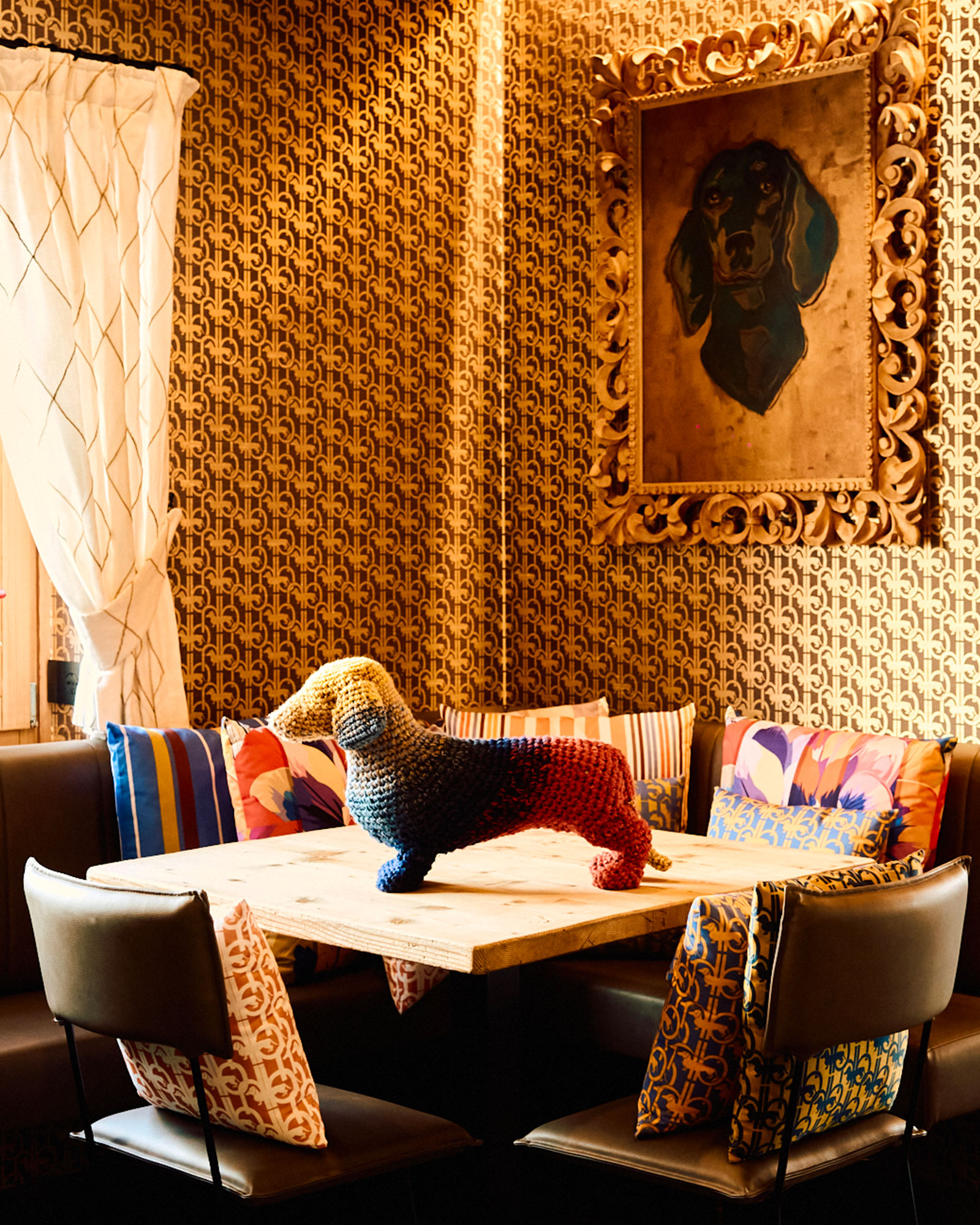 Scultura di bassotto colorato su tavolo in ambiente decorato con cuscini stampati e quadro del cane.