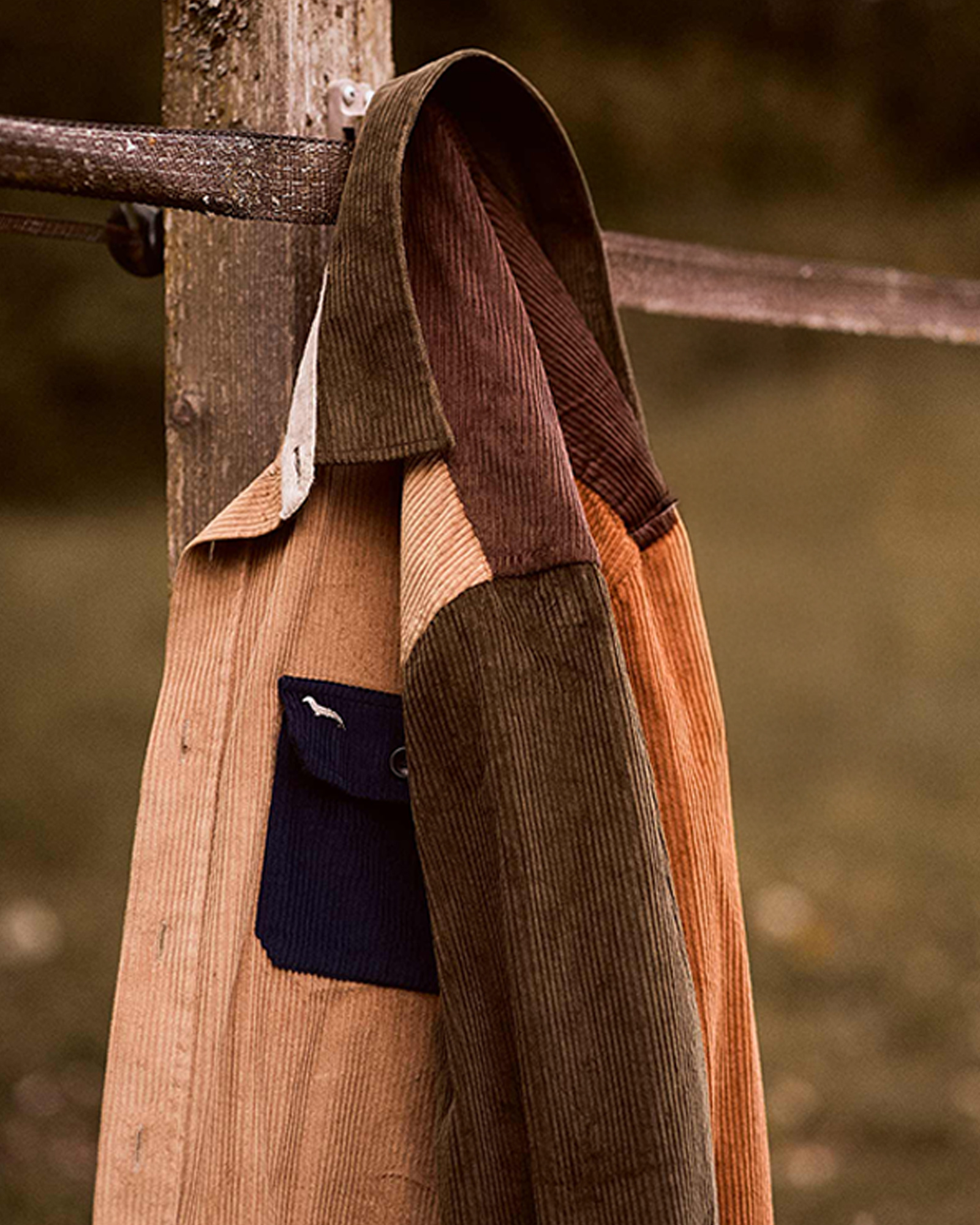 Dettaglio di overshirt in velluto a coste multicolore appesa a una staccionata.