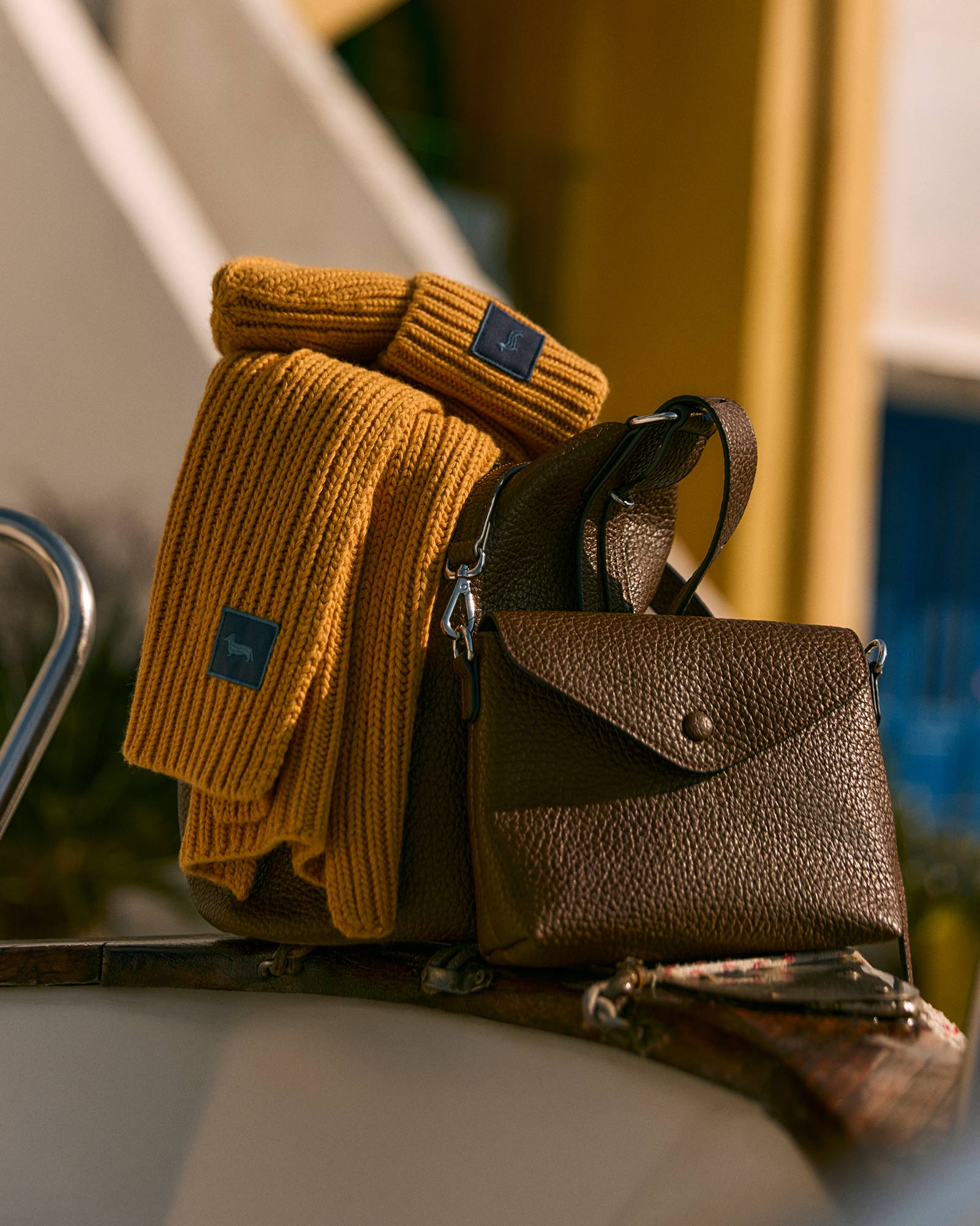 Brown leather bag and yellow knit scarf placed on a boat.