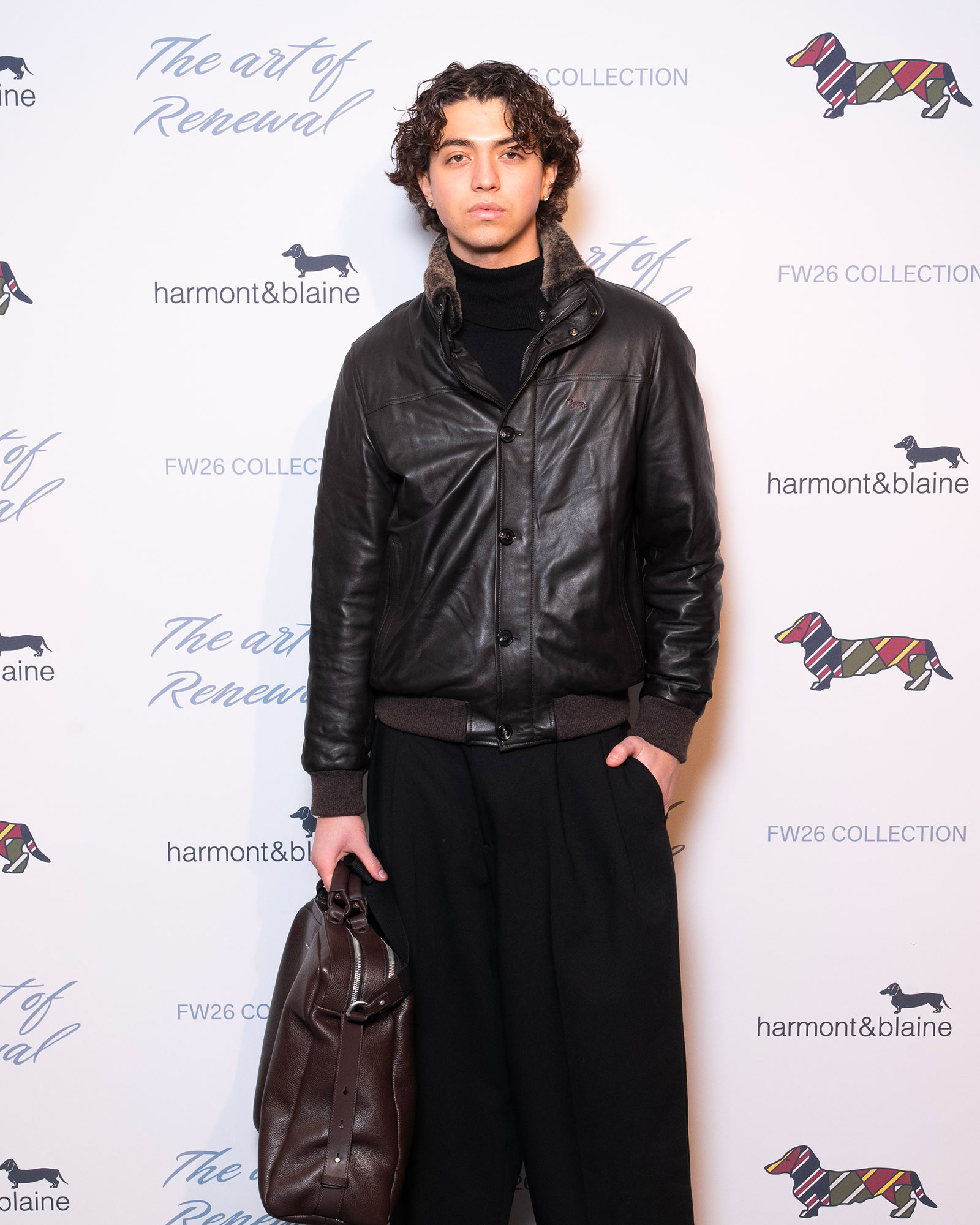 Uomo con giubbotto in pelle nero e pantaloni larghi scuri con borsa