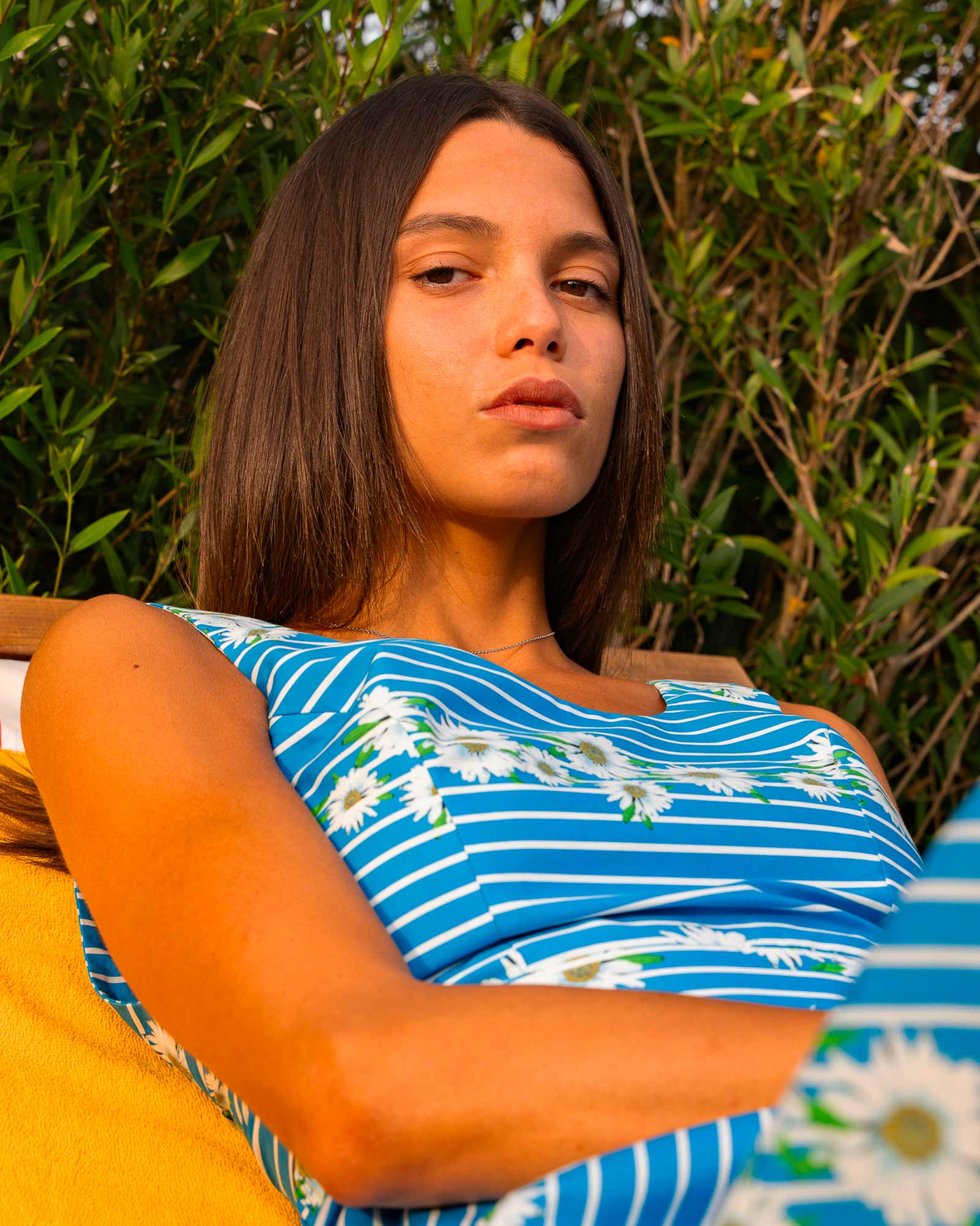 Woman wearing a blue and white striped top with daisy print, relaxing outdoors against a lush green background — fresh and confident summer style.