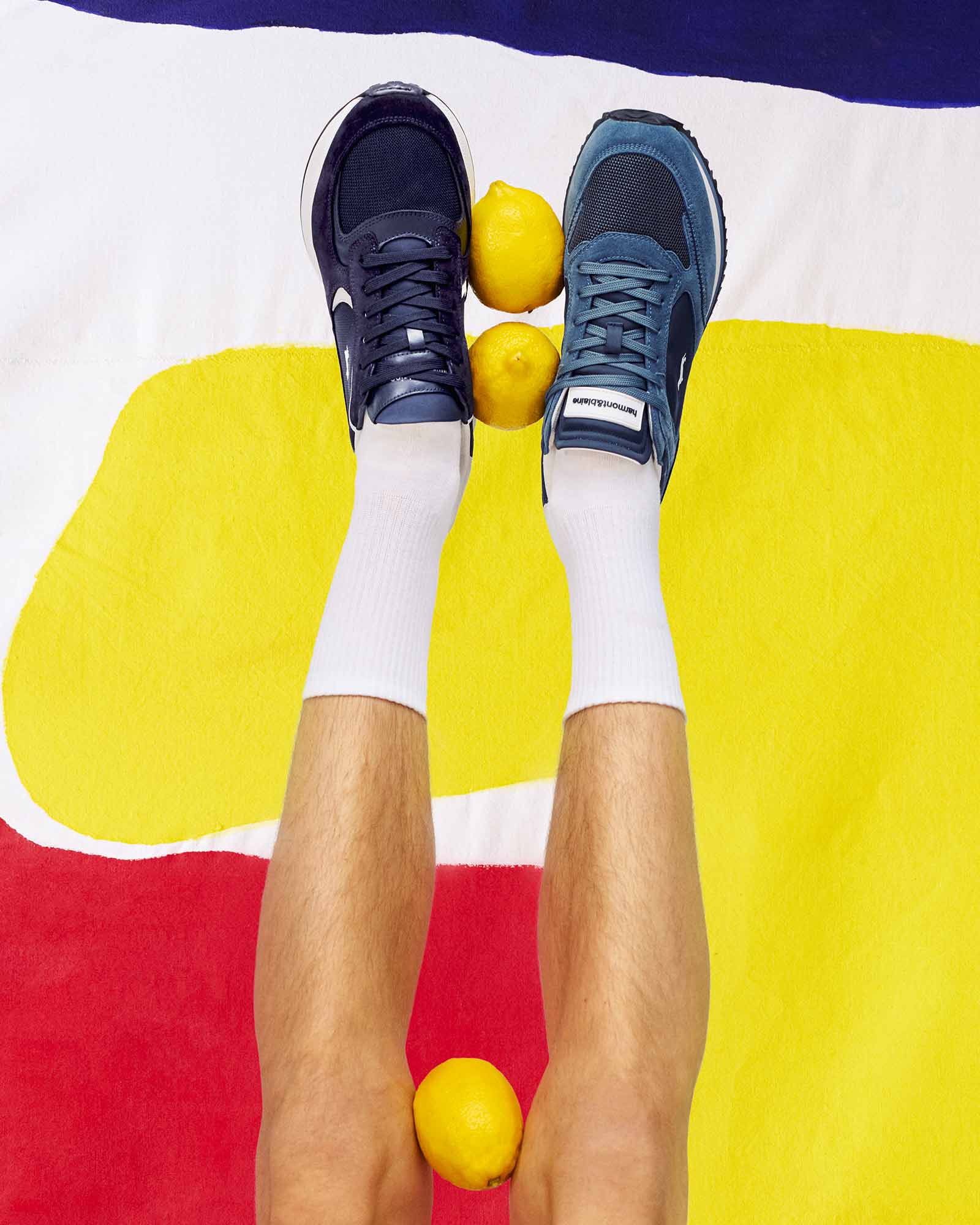 Playful image of legs raised in the air with mismatched blue sneakers and white socks, balancing lemons against a colorful background — fun and bold HB Mood.