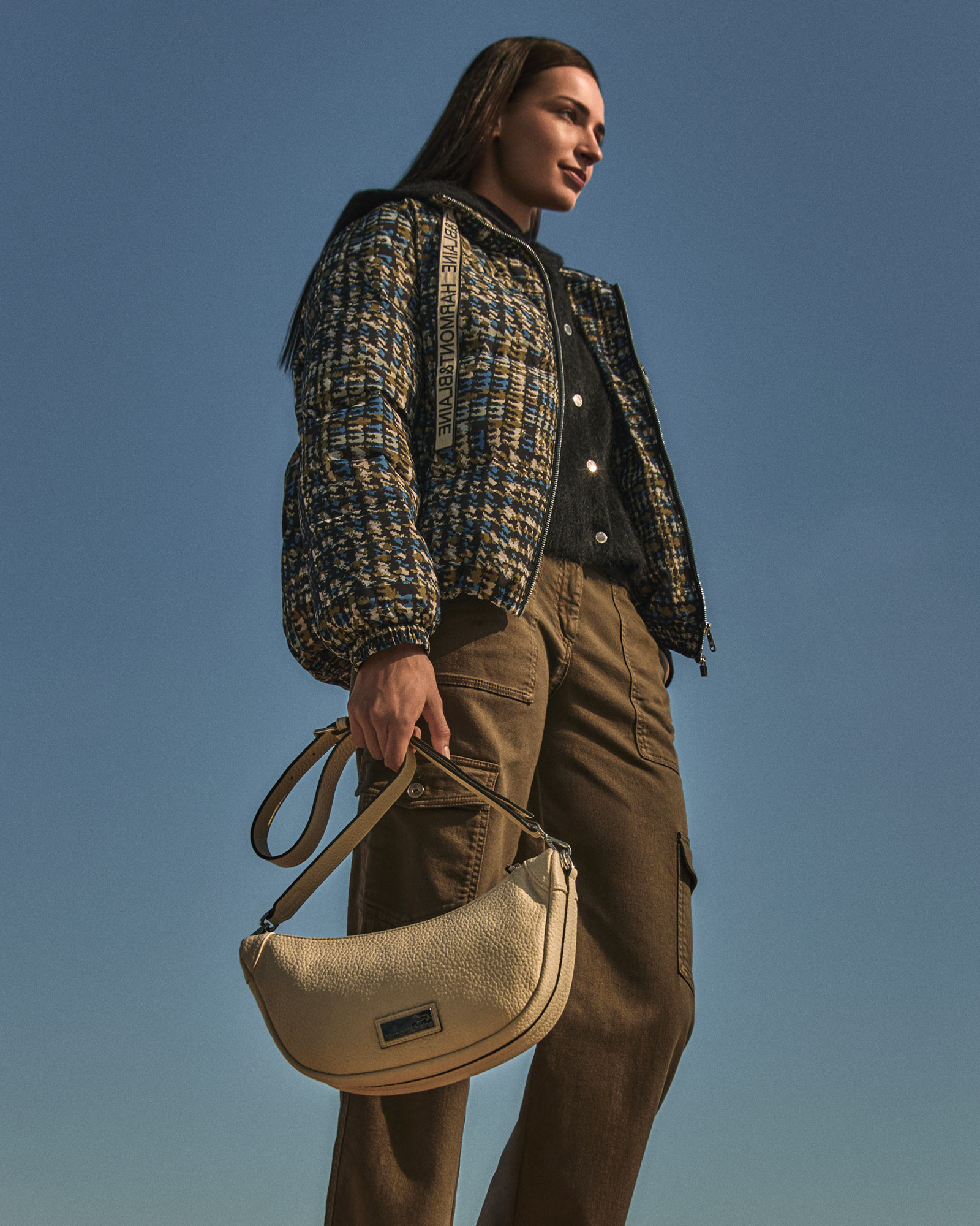 Woman wearing a patterned jacket with brown cargo trousers and light handbag.
