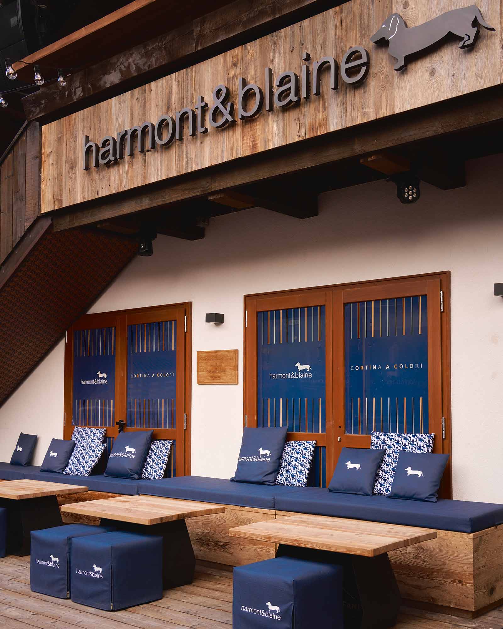 Exterior view of the Harmont & Blaine boutique with wooden details, navy blue decor and branded cushions — welcoming atmosphere of the “Cortina a Colori” event.