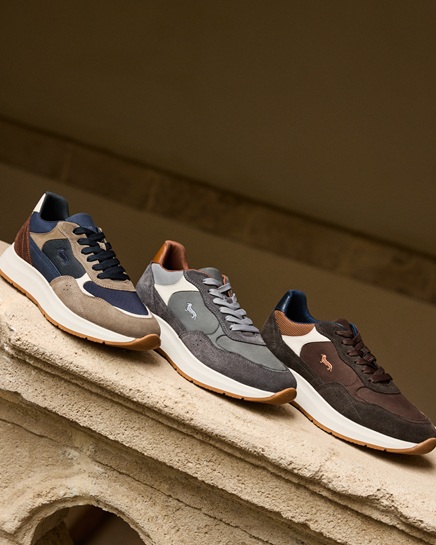 The promotional image for the Single's Day Men's campaign showcases a selection of three men's athletic sneakers arranged along a stone ledge. Crafted in color-blocked suede and technical fabric featuring the iconic embroidered Dachshund on the side, the models are presented in refined colorways of beige/navy, grey/charcoal, and brown/mocha.
