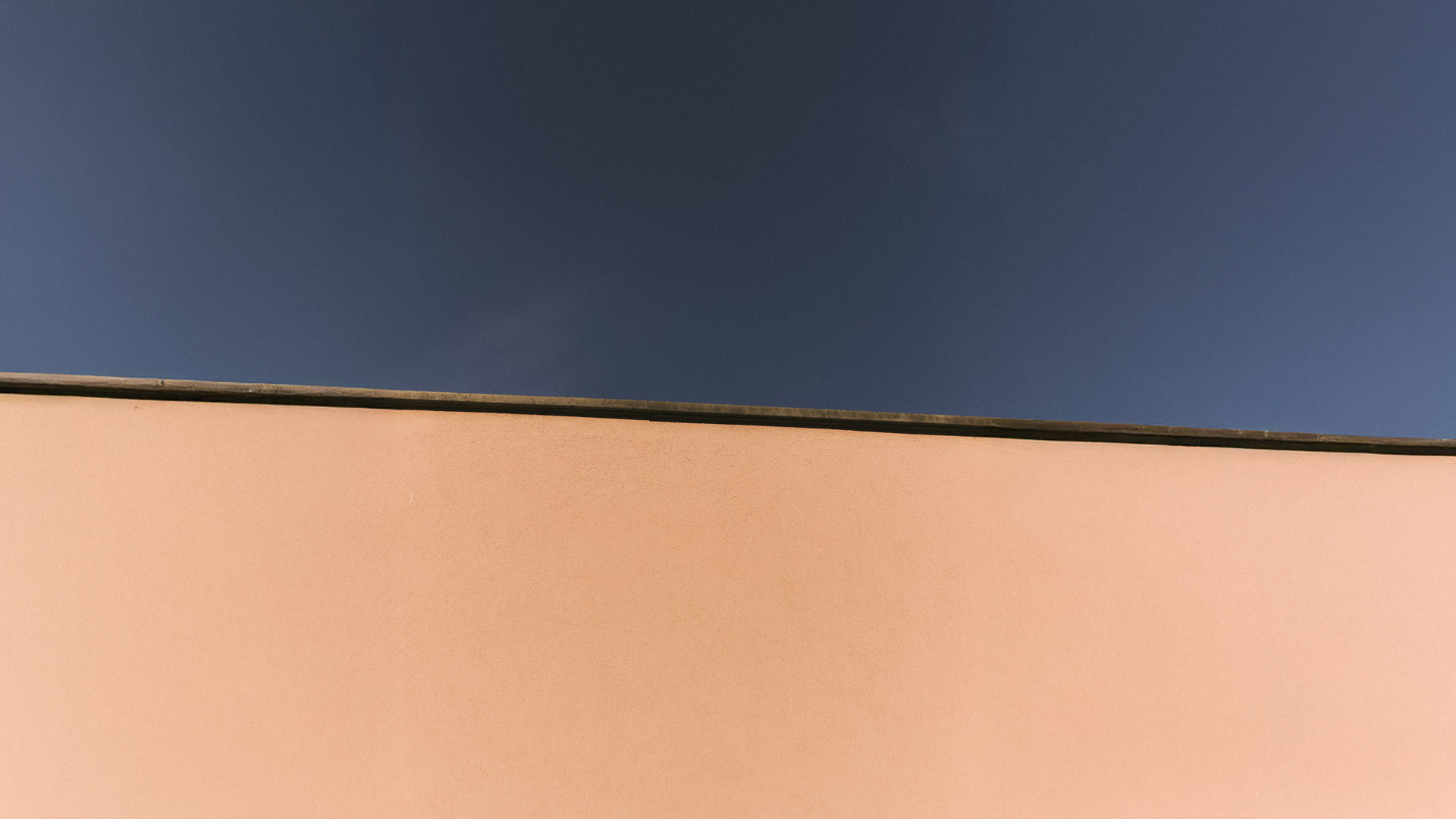 Parete rosa illuminata con orizzonte di cielo blu.