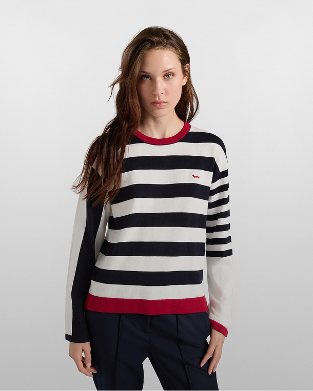 Woman wearing a navy blue and white horizontal striped sweater with red ribbed trims and an embroidered dachshund logo on the chest, paired with dark trousers.