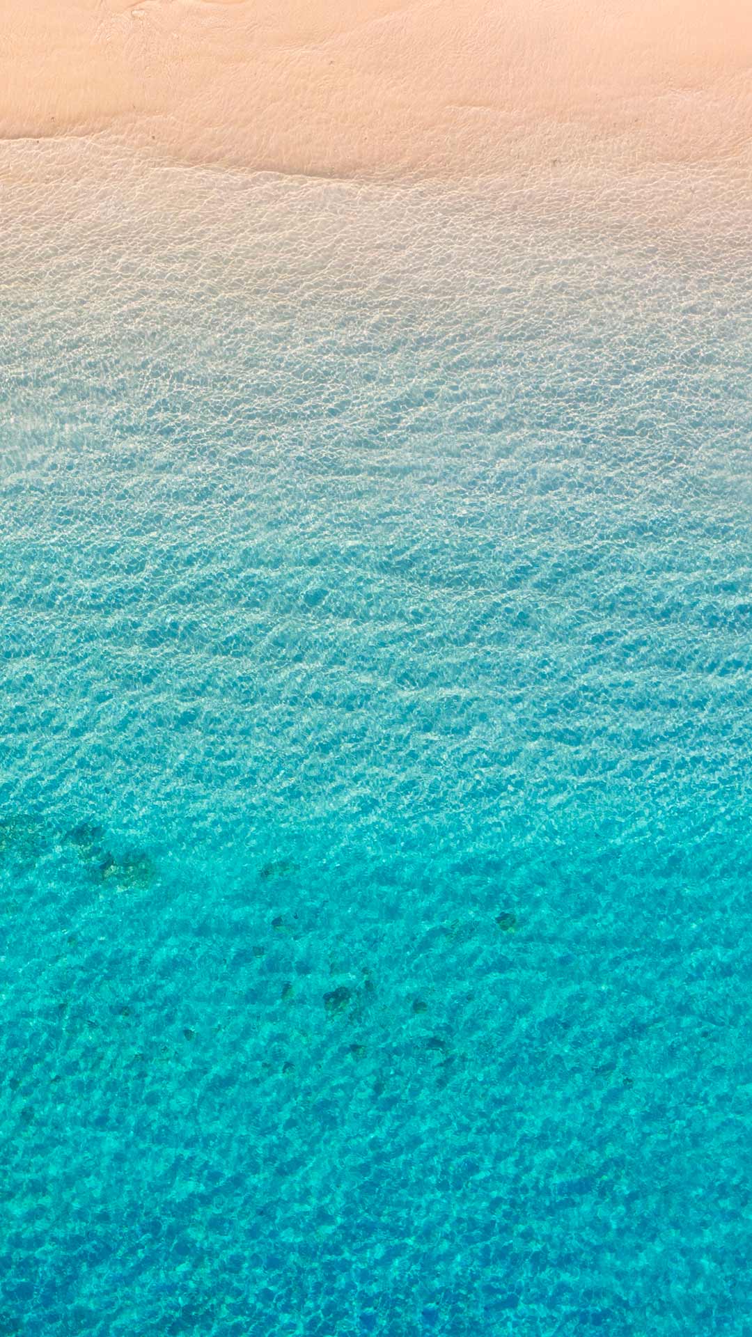 Spiaggia con sabbia dorata e mare turchese cristallino vista dall’alto.