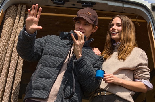The promotional image for the Single's Day campaign shows a smiling young couple looking at the view from inside an outdoor-style van. The man is wearing a dark grey puffer jacket and a brown Harmont & Blaine cap while holding binoculars, while the woman beside him wears a beige sweater and holds a blue mug.