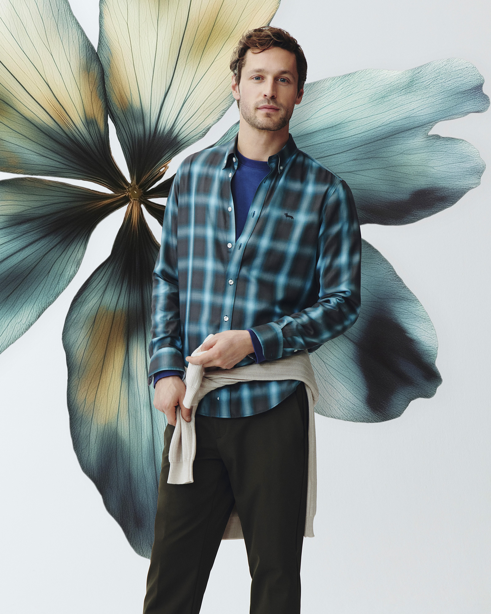 Man in blue and green check shirt, blue sweater underneath and dark trousers