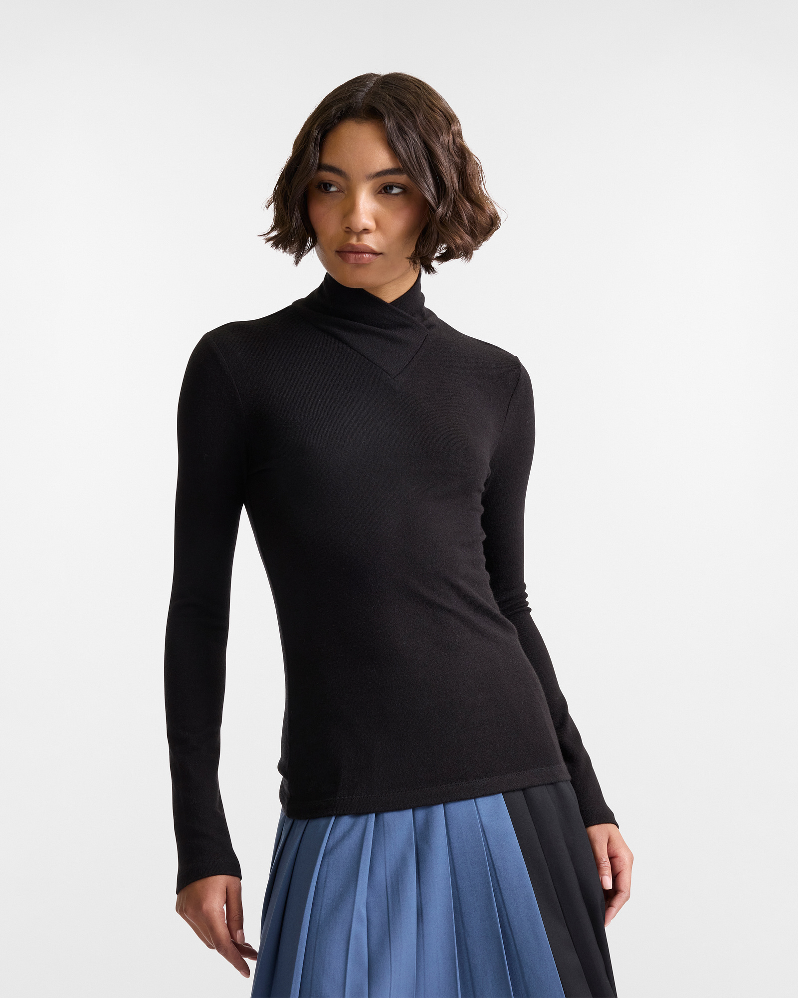 Woman in black long-sleeve turtleneck, paired with pleated blue and black skirt