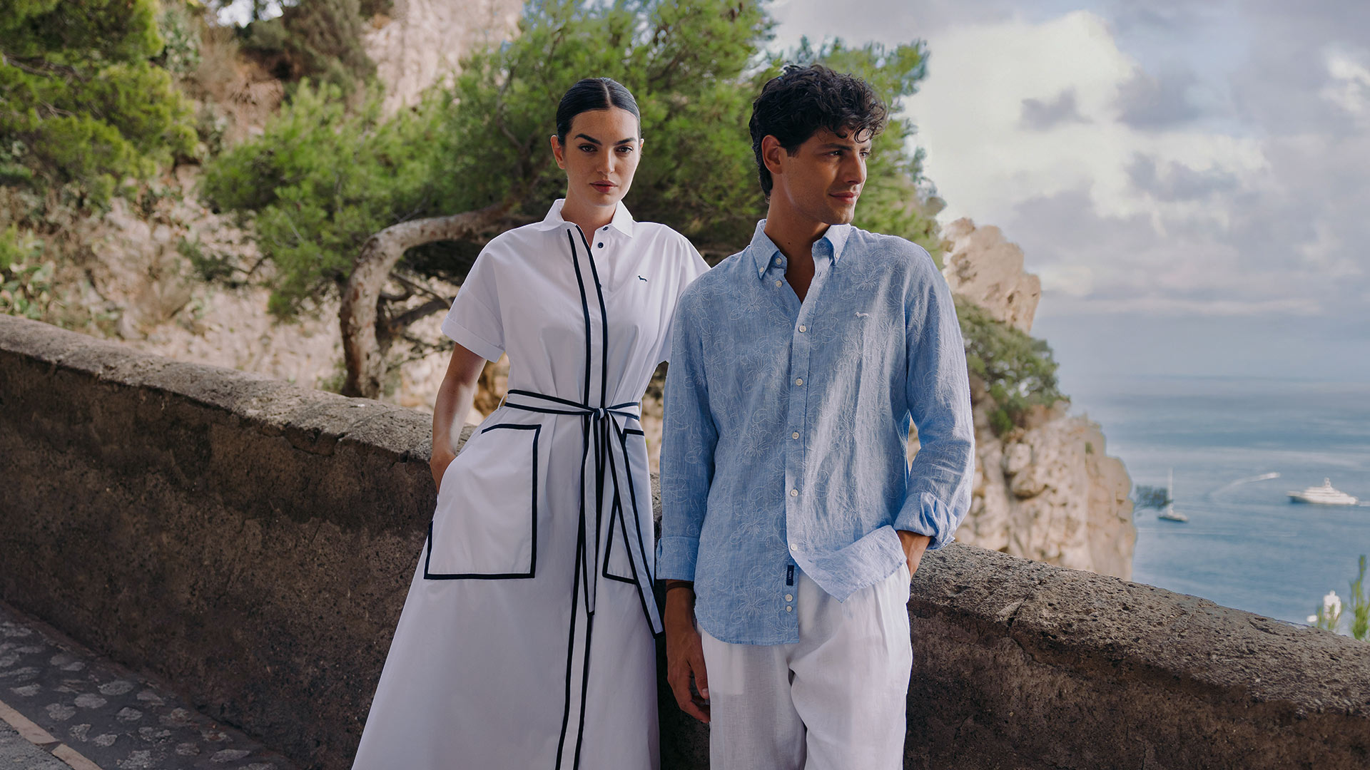Woman in white dress with black trim next to man in light blue shirt and white trousers