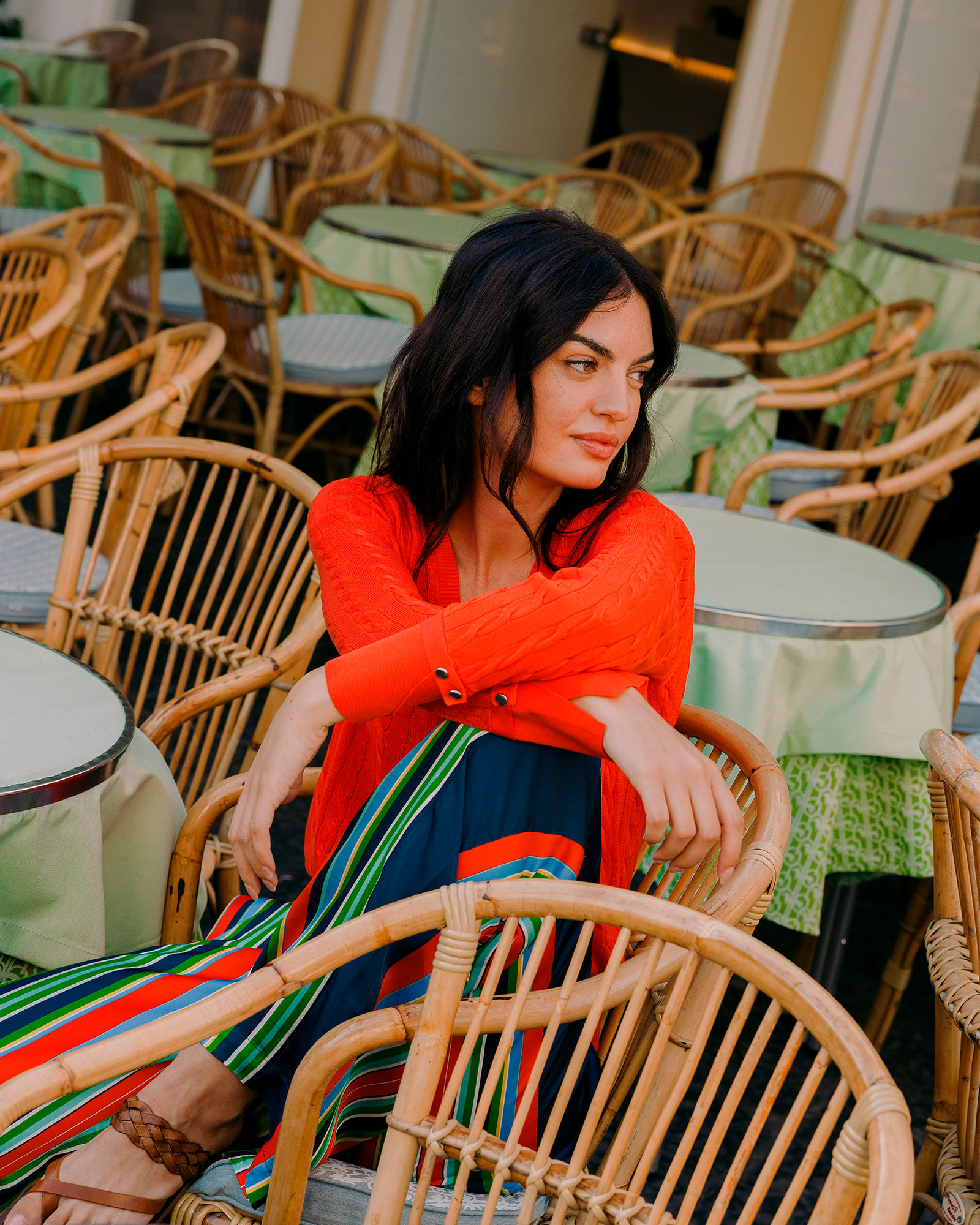 Woman in red cardigan and multicolor striped trousers sitting at a café
