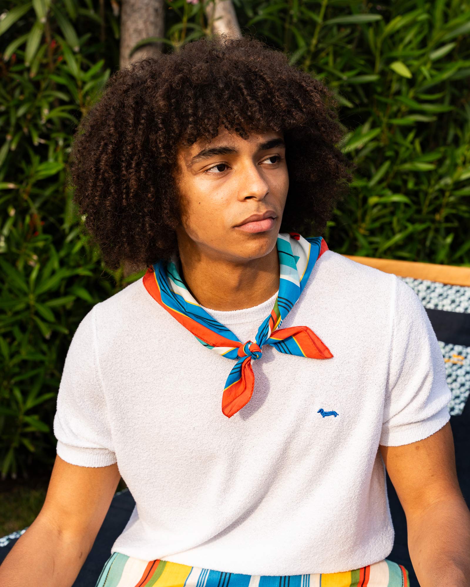 Man wearing a white terry tee and colorful scarf, in a casual summer look.