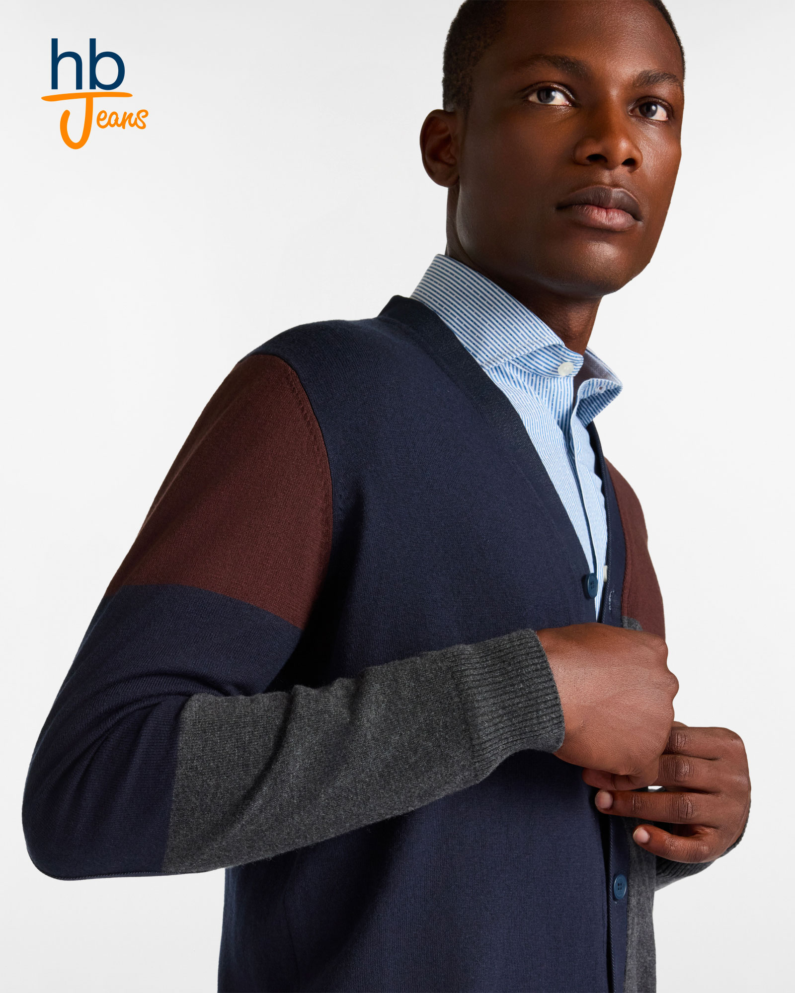 Uomo con cardigan a blocchi di colore blu, marrone e grigio e camicia azzurra a righe.